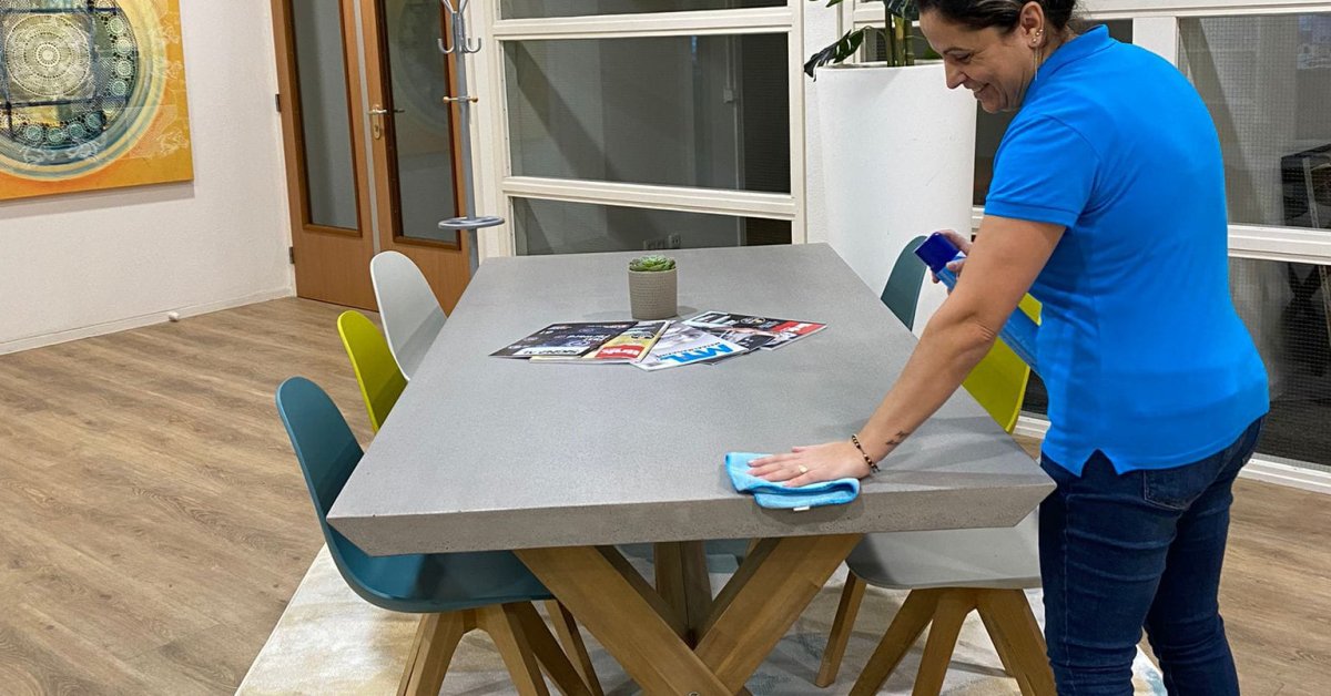 Schoonmaker veegt een vergadertafel schoon in een lichte kantoorruimte.